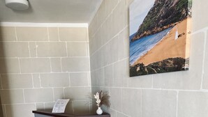 Un mostrador de recepción con un menú, un jarrón con plantas secas y una pintura de un paisaje costero en la pared.