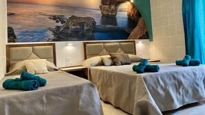 Habitación de hotel con dos camas, un amplio mural con un atardecer sobre el océano y una vista por una ventana enmarcada por un arco de roca.