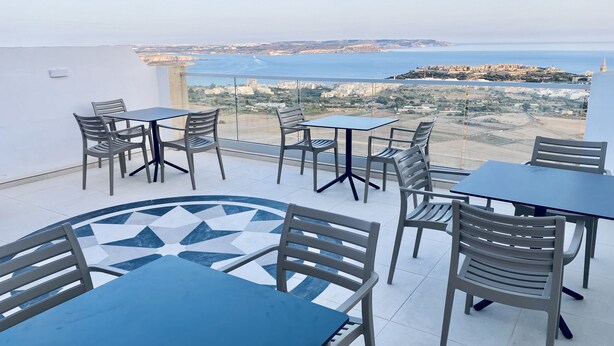 Una terraza con mesas y sillas, con vistas al mar y edificios a la distancia.