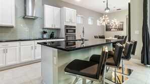 A modern kitchen with white cabinets, stainless steel appliances, and a central island with bar stools. - Lovely 5 Bed Family Pool Home in Reunion-7786LL (Kissimmee)