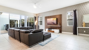 A modern living room with a sectional sofa, a flat-screen TV, and a patterned wall. - Lovely 5 Bed Family Pool Home in Reunion-7786LL (Kissimmee)