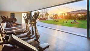 Un gimnasio con cintas de correr y elípticas, una zona de piscina con sillones de descanso y vistas al atardecer.