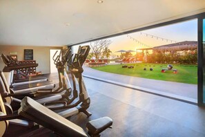 Academia com esteiras e elípticos, área de piscina com espreguiçadeiras e vista para o pôr do sol.