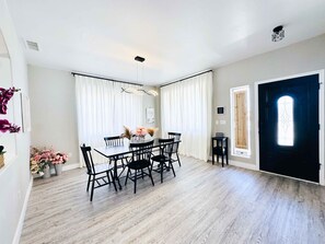 A dining area with a wooden table and chairs, white curtains, and a vase with flowers. - Desert Blooms: Heated Pool & Spa - Winter Oasis (Tucson)