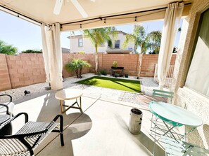 A covered patio area with a small lawn, seating arrangements, and a brick wall in the background. - Desert Blooms: Heated Pool & Spa - Winter Oasis (Tucson)