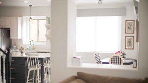 Una cocina moderna con armarios blancos, una isla central y un comedor con mesa y sillas a cuadros.