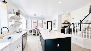 Una cocina moderna con armarios blancos, una isla negra y un comedor con mesa y sillas.