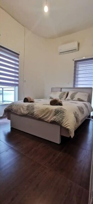 Relax in this serene bedroom with a large bed and two windows with blinds.