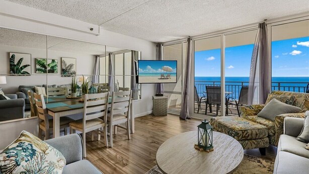 Un salón moderno con un televisor grande, suelo de madera y un balcón con vistas al mar.