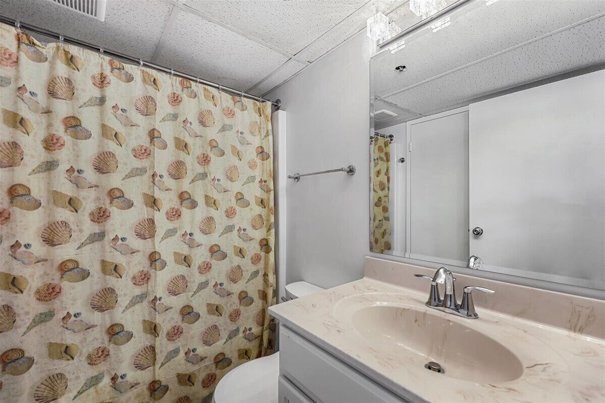 A bathroom with a shower curtain featuring a sea shell pattern, a large mirror, and a sink with a marble countertop.