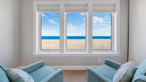 Ein Zimmer mit großem Fenster mit Blick auf einen Strand, zwei blaue Sessel und ein Teppichboden.