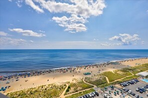 Een strand met veel parasols en mensen, een parkeerplaats en een heldere lucht.