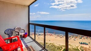 A balcony with a view of a beach, plastic chairs, and a small table. - Golden Sands 1617 by Seaside Vacations & Sales (Ocean City)
