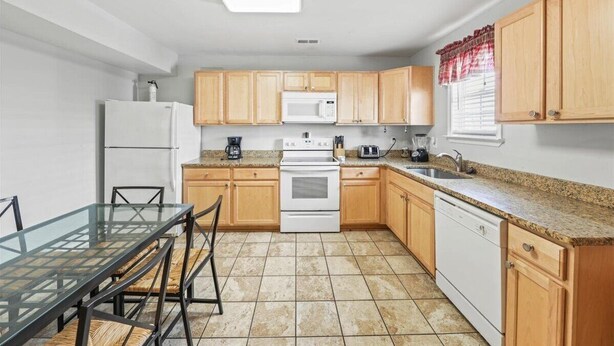 A compact kitchen with wooden cabinets, a white refrigerator, a microwave, an oven, and a dishwasher.