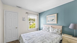 A bedroom with a bed, a nightstand, a window with a view, and a door.