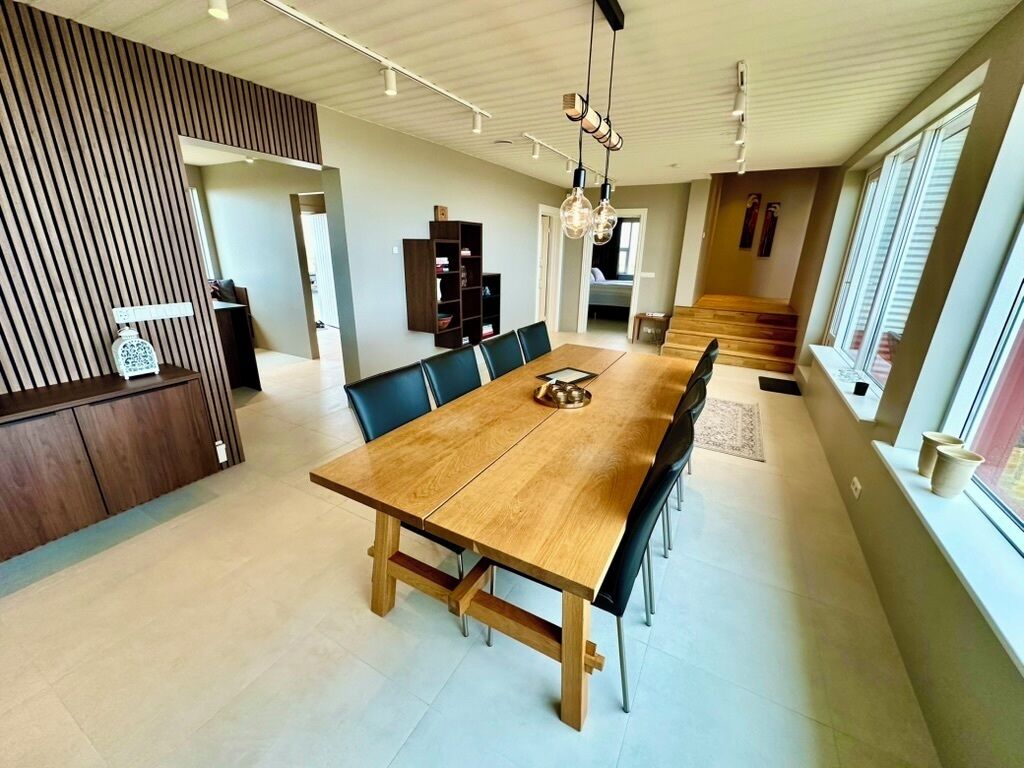 Un comedor amplio con una mesa y sillas de madera, una estantería y una escalera que sube a otro nivel.