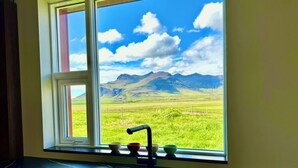 A kitchen with a window view of a grassy field and mountains.
