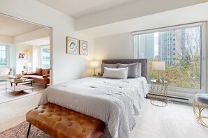 Un dormitorio moderno con una cama grande, un banco y vistas de edificios altos, además de un paisaje urbano.