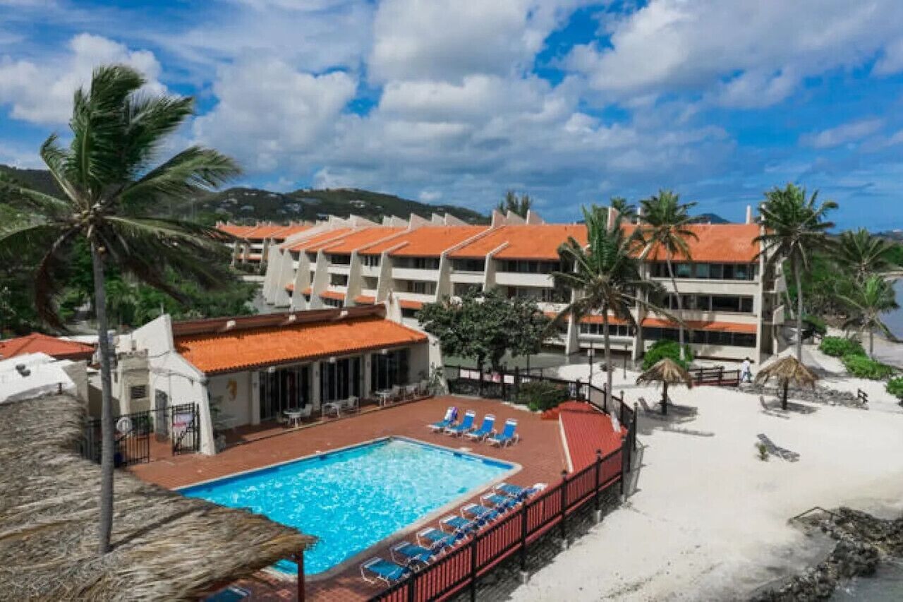 Un hôtel doté d’une piscine, de chaises longues installées sur la plage et de palmiers.