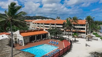 Un hôtel doté d’une piscine, de chaises longues installées sur la plage et de palmiers.