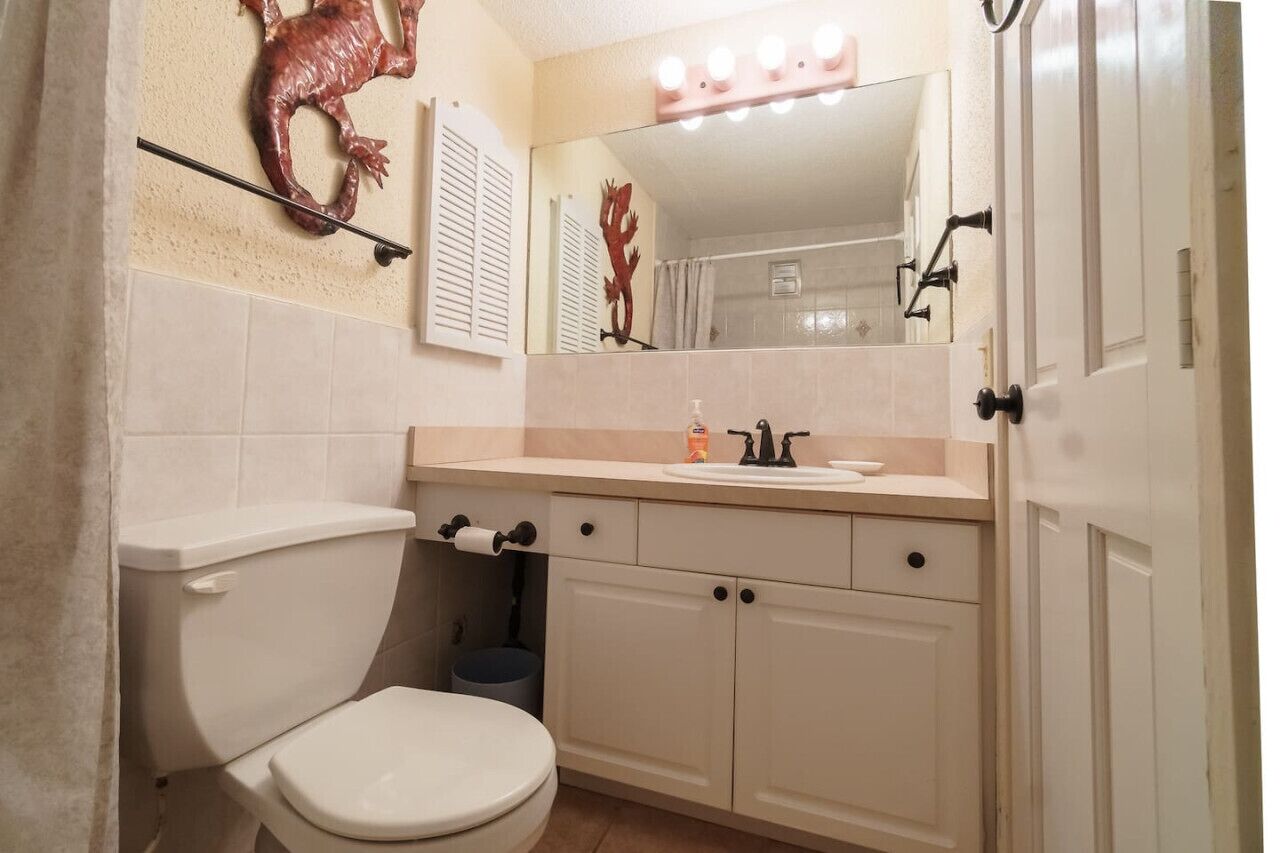 A bathroom with a toilet, sink, mirror, and cabinets.