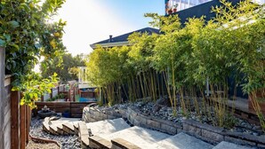 Un jardín con un sendero de piedra, plantas de bambú y una valla de madera.