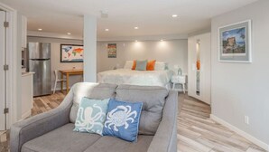 Un apartamento moderno con un sofá gris, una cama con almohadas naranjas, una zona de cocina y una mesa de comedor.