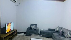 A living room with a grey sofa, a coffee table, and a TV on a wooden stand. - Furnished Studio, kotto, Douala. (Région du Littoral)