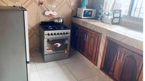 A kitchen with a gas stove, oven, and microwave. There is a window with curtains and a cabinet with a microwave on top. - Furnished Studio, kotto, Douala. (Région du Littoral)