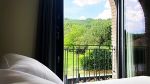 A hotel room with a large bed, a window with a view of a green landscape, and a balcony with a metal railing. - Agriturismo I Tre Colli  (Solignano)