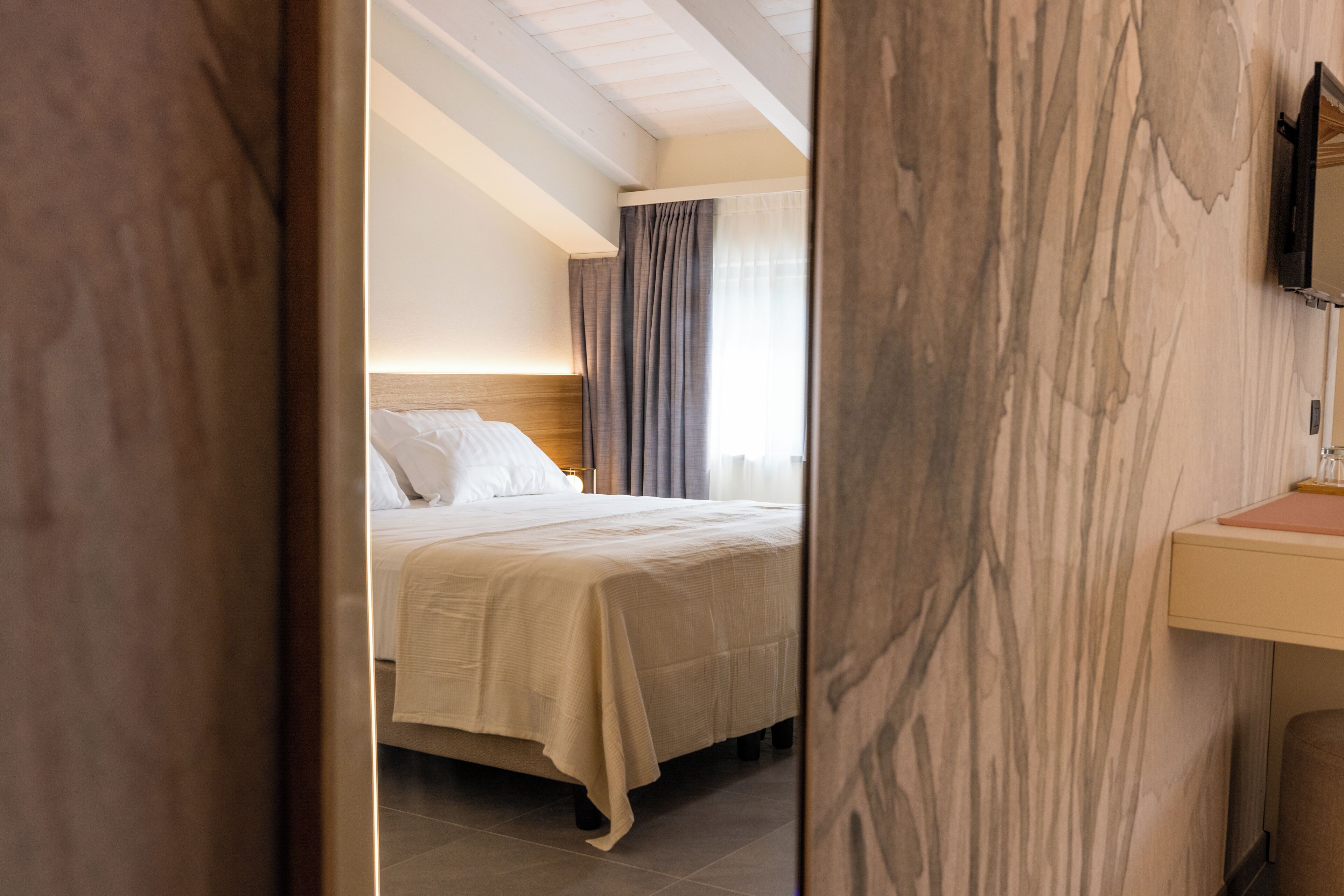 Une chambre d’hôtel avec un lit, une table de chevet, un miroir et une fenêtre avec des rideaux.
