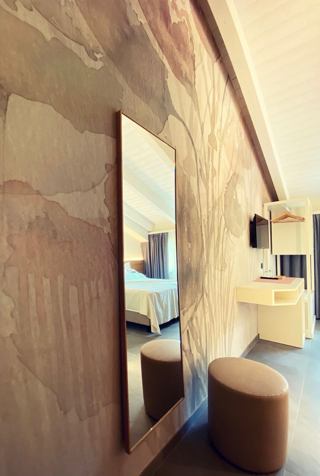 Une chambre d’hôtel moderne, dotée d’un grand miroir, d’un lit, d’un petit pouf rond et d’un bureau avec un téléviseur.