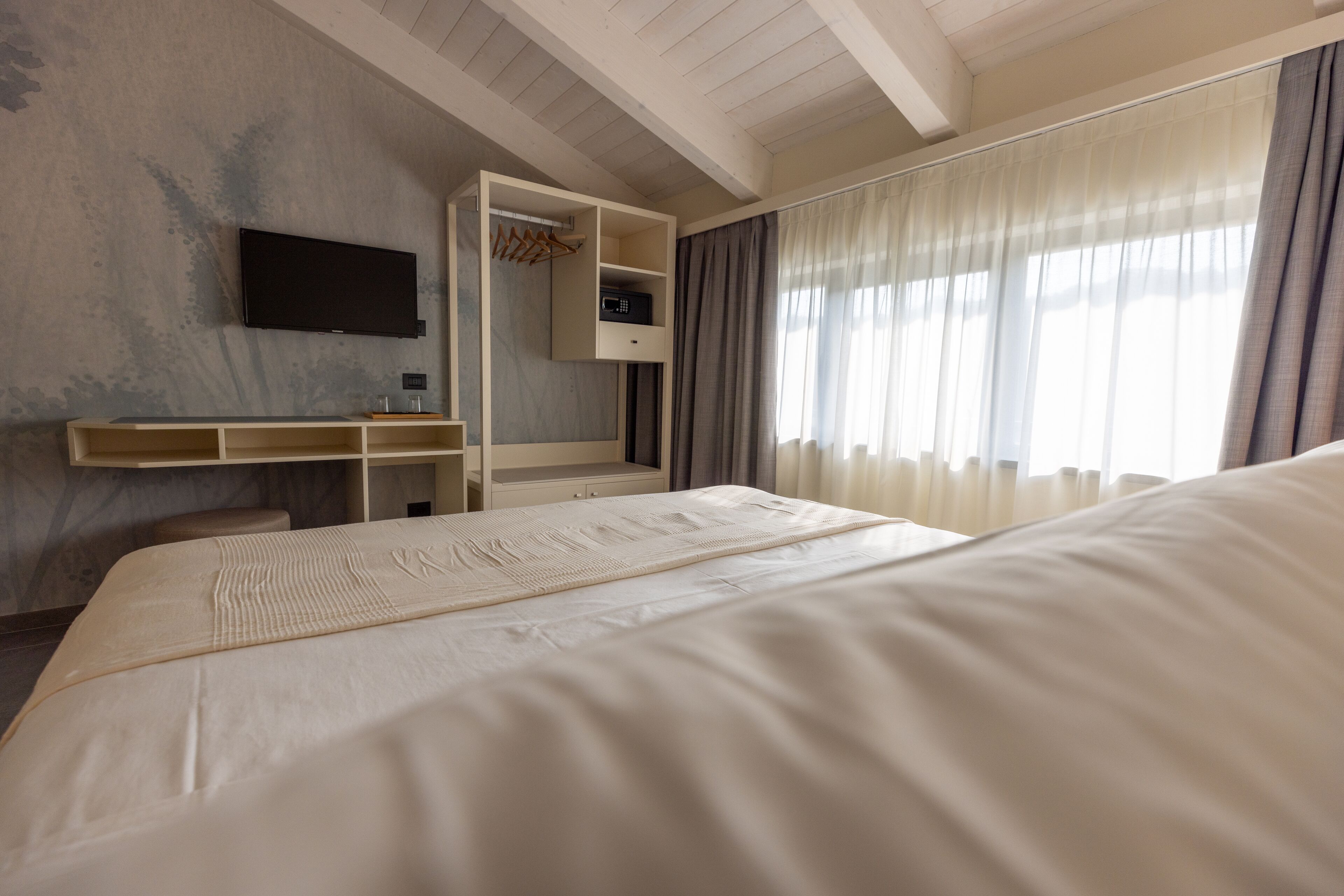 Ein Hotelzimmer mit Bett, Schreibtisch mit Stuhl, Wandfernseher und einem fenster mit Vorhängen.