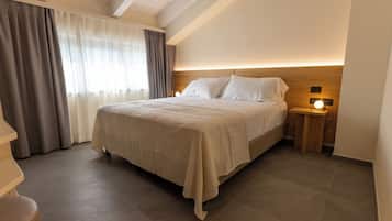 A neatly arranged bedroom with a large bed, a bedside table with a lamp, and a window with curtains.