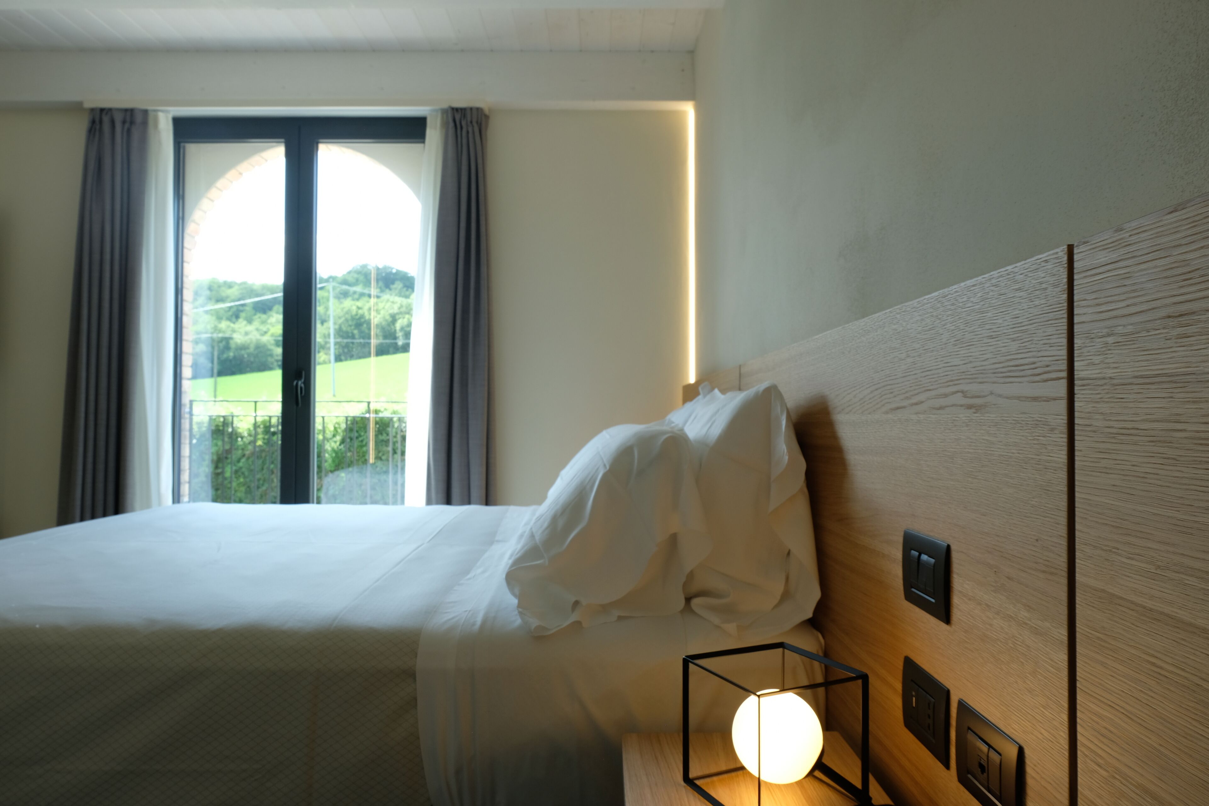 A hotel room with a bed, a bedside lamp, and a view of a green landscape through a window.