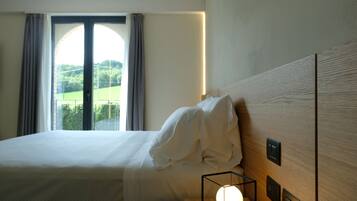 A hotel room with a bed, a bedside lamp, and a view of a green landscape through a window.