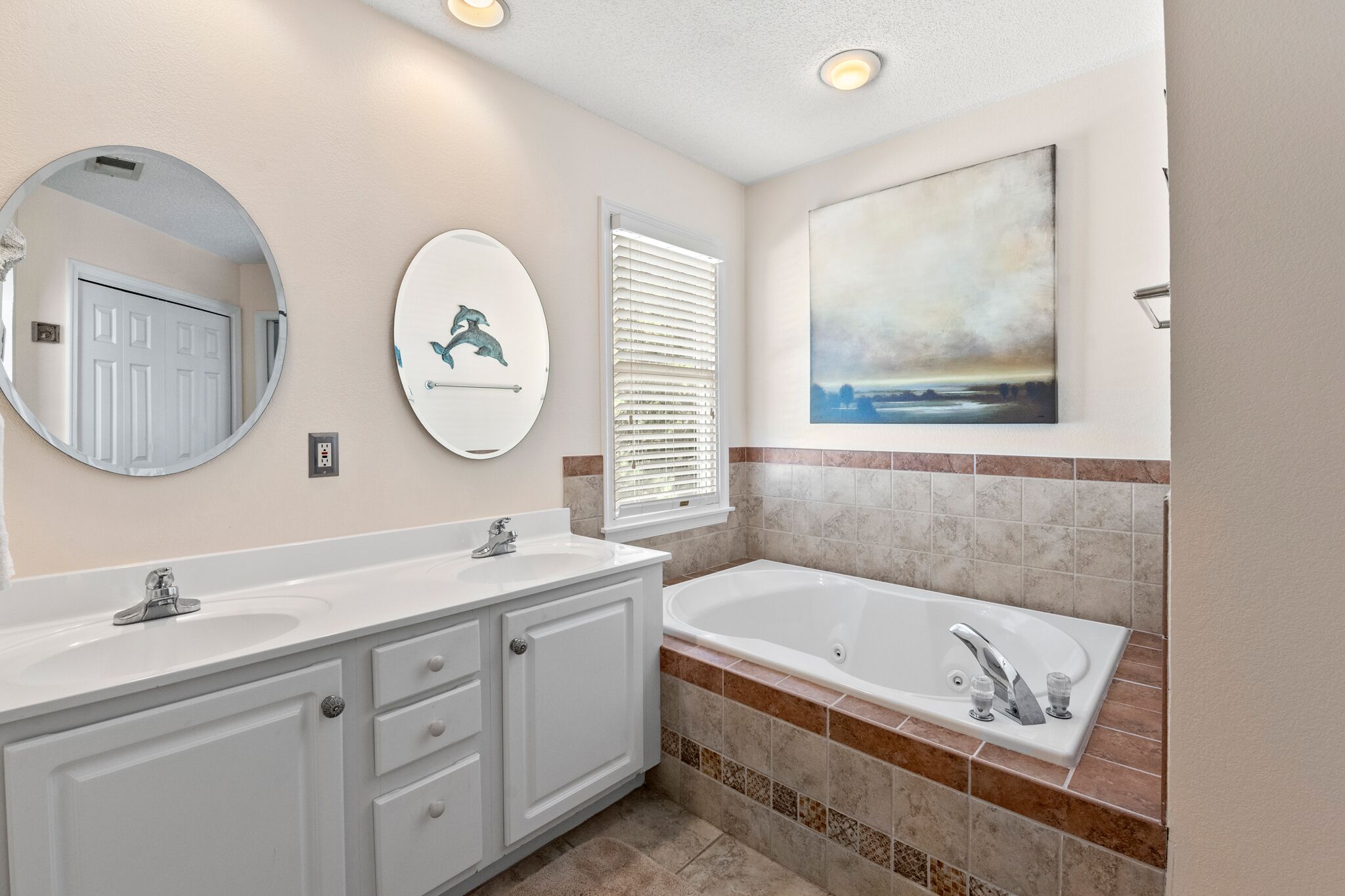A bathroom with a double sink vanity, a large mirror, a bathtub, and a window with blinds.