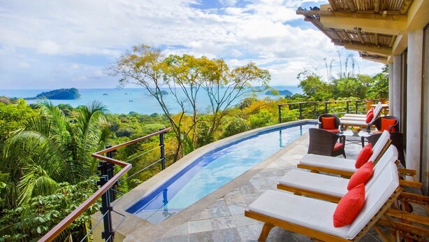 A poolside area with lounge chairs and a view of the ocean and a tropical landscape. - 7 bedrooms Manuel Antonio and Ocean view Private Pool and rooftop Jacuzzi (Puntarenas Province)