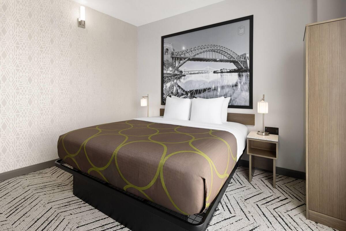 Habitación de hotel con una cama, una mesita de noche, una lámpara, un armario y una pared con un diseño geométrico.