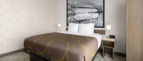 A hotel room with a bed, a nightstand, a lamp, a wardrobe, and a wall with a geometric pattern.