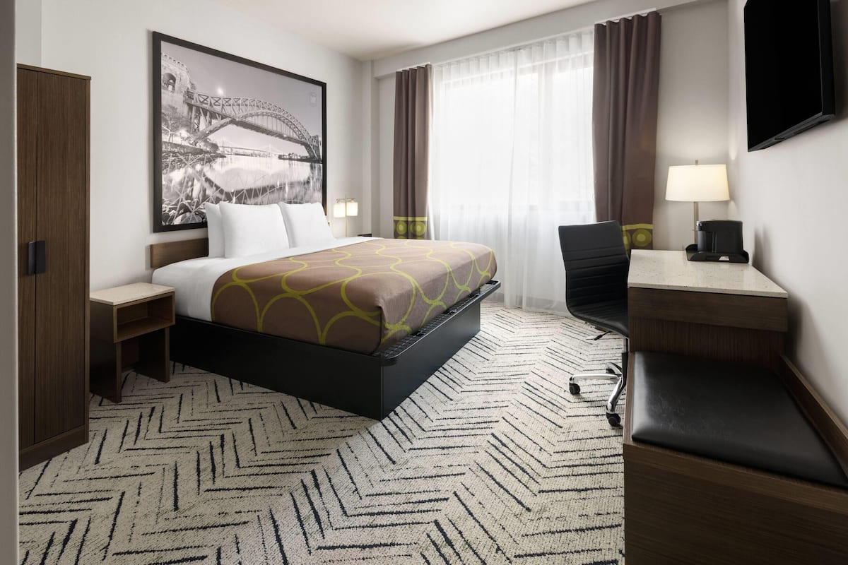 Habitación de hotel con cama, escritorio, silla y un cuadro grande en la pared.