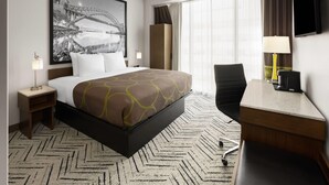 Ein Hotelzimmer mit Bett, Schreibtisch, Stuhl, Fernseher, Kleiderschrank und einem großen Fenster mit Vorhängen.