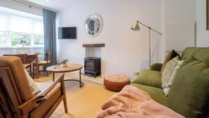 A living room with a sofa, a wooden chair, a round table, a fireplace, a television, and a window with curtains. - Henry Bell 2 bed in Helensburgh Near Loch Lomond (Helensburgh)
