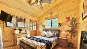 A wooden cabin bedroom with a bed, dresser, and a fireplace. - Western theme! | Amazing Spa, Fireplace and Deck! (Overgaard)