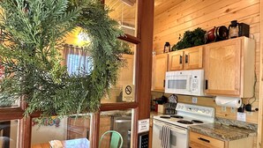 A cozy kitchen with wooden cabinets, a microwave, an oven, and a dining area with a table and chairs. - Western theme! | Amazing Spa, Fireplace and Deck! (Overgaard)