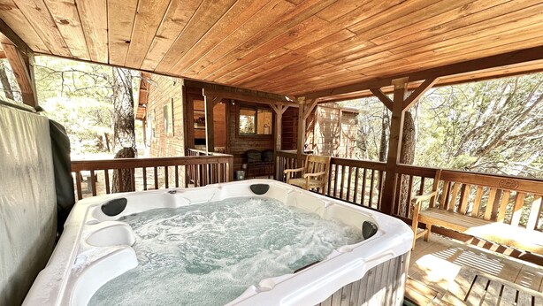 A wooden deck with a hot tub, wooden chairs, and a wooden cabin in the background. - Western theme! | Amazing Spa, Fireplace and Deck! (Overgaard)