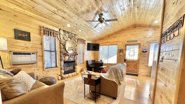A cozy log cabin interior with a fireplace, wooden walls, a ceiling fan, and a stone fireplace surround. - Stoney Creek | Peaceful Cabin, Couples Retreat (Overgaard)