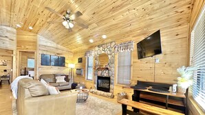 A cozy log cabin interior with a fireplace, a television mounted on the wall, and a comfortable seating area with a sofa and a bench. - Stoney Creek | Peaceful Cabin, Couples Retreat (Overgaard)