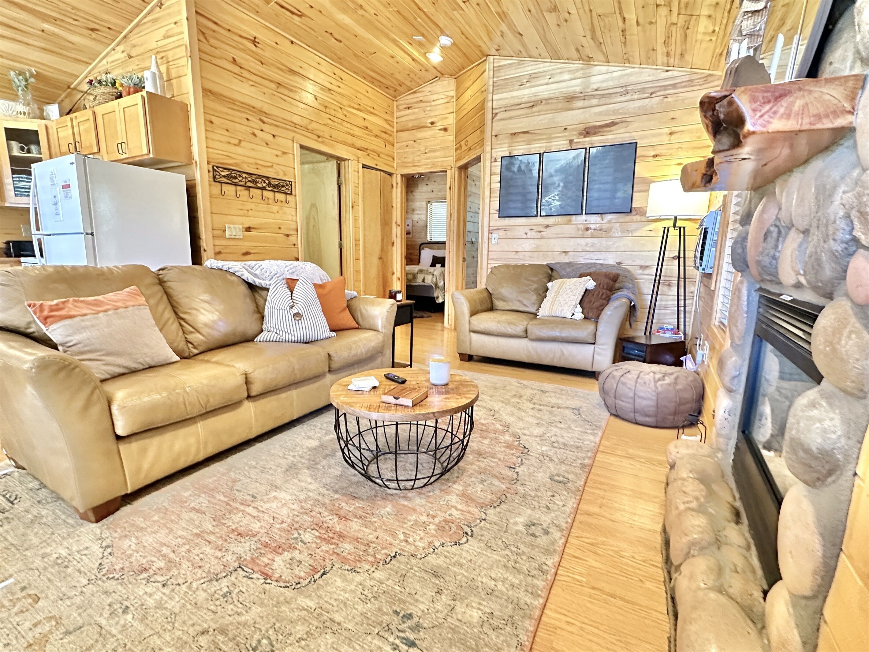 A cozy wooden cabin interior with two leather sofas, a round coffee table, and a fireplace.