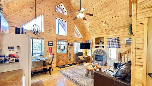A spacious cabin with a high ceiling, wooden walls, a fireplace, a sofa, a dining area, and a kitchen. - Juniper Grove | Loft & Personal Hot Tub! (Overgaard)
